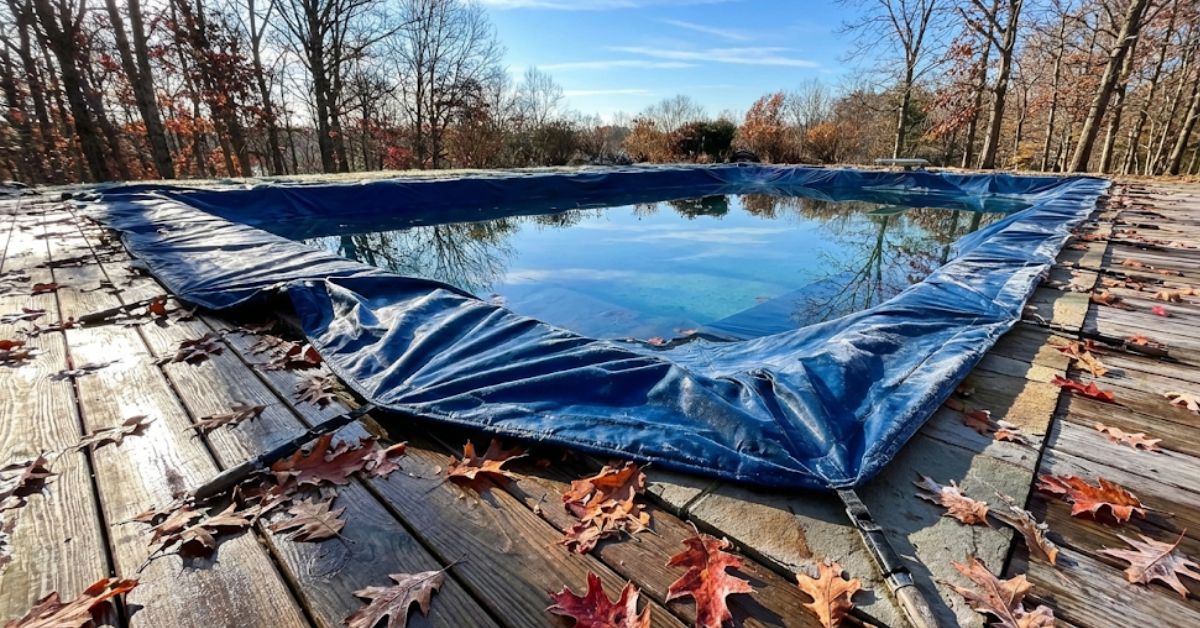 A backyard swimming pool being prepared for winter with a blue cover.
