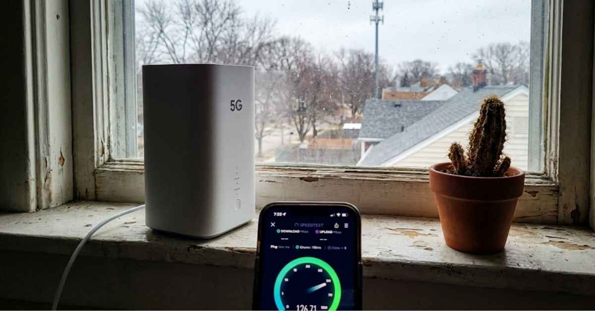 A 5G home internet gateway on a wooden windowsill showing a speed test on a phone.