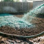 Professional hydro-seeding slurry being sprayed on dark soil in a backyard.