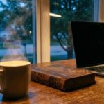 A dark home office with a closed laptop and a warm cup of tea at night.