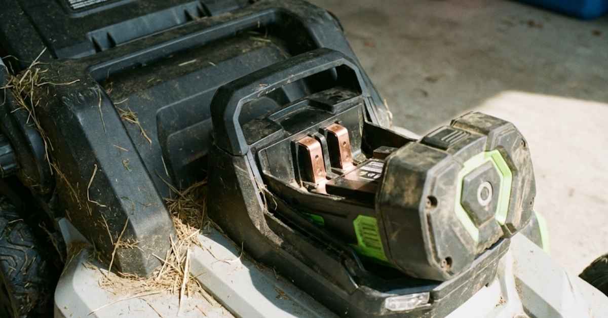 Close-up of a high-voltage lithium battery being inserted into a lawn mower.