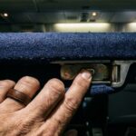 Close-up of a hand pressing the hidden button under an airplane aisle armrest.
